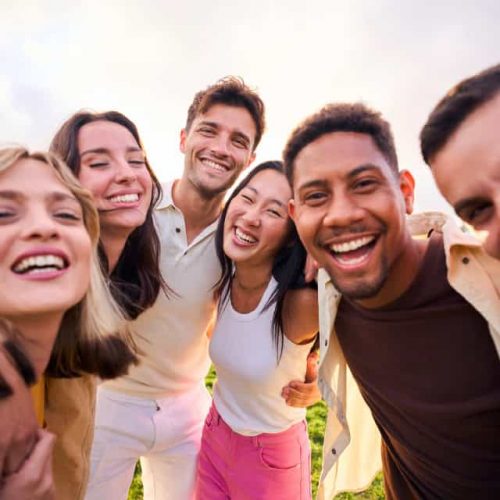 Multiracial people happy group smiling at camera for photo outdoors on sunny day. Diverse laughing young friends enjoy together hugging. Positive friendship relationships in diverse community.
