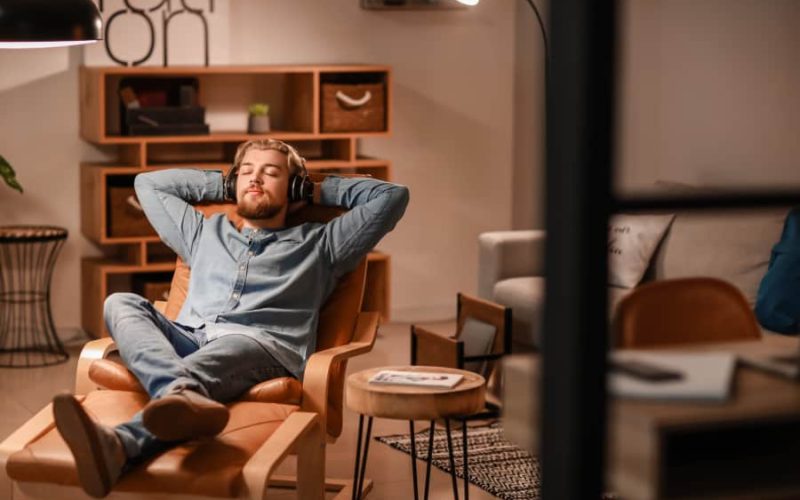 Young man listening to music while sitting in armchair at home